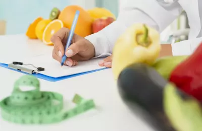 Professionnel de santé rédigeant une ordonnance nutritionnelle, avec des légumes et fruits.